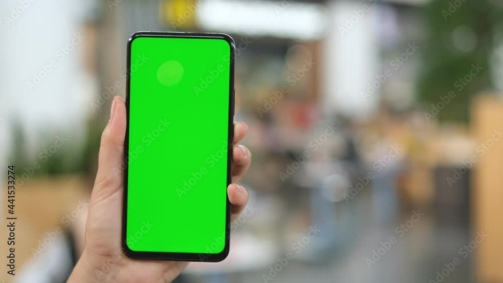 Mall. Shopping center. Back view of brunette holding chroma key green screen smartphone watching content. Shopping online. Gadgets and contemporary people concept. Mall. Shopping center. Back view of brunette holding chroma key green screen smartphone watching content. Shopping online. Gadgets and contemporary people concept.