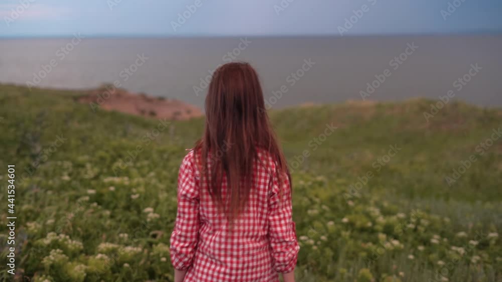 The back view of a schoolgirl girl walks on a green field in summer. Without a face. The back view of a schoolgirl girl walks on a green field in summer. Without a face.
