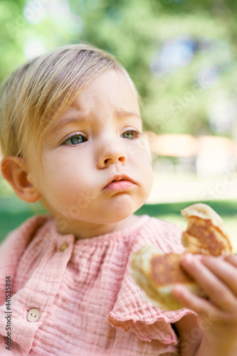 Little girl holds a bitten pancake in her hand. Portrait
