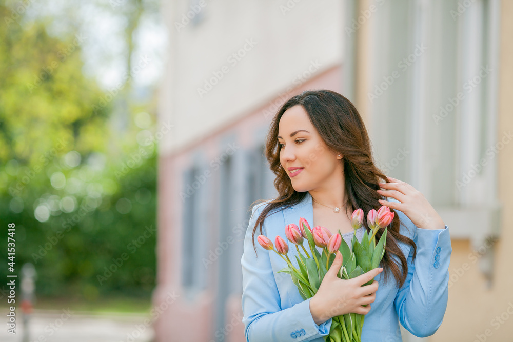 Portrait of a beautiful young woman in a blue suit with a bouquet of tulips. Spring.