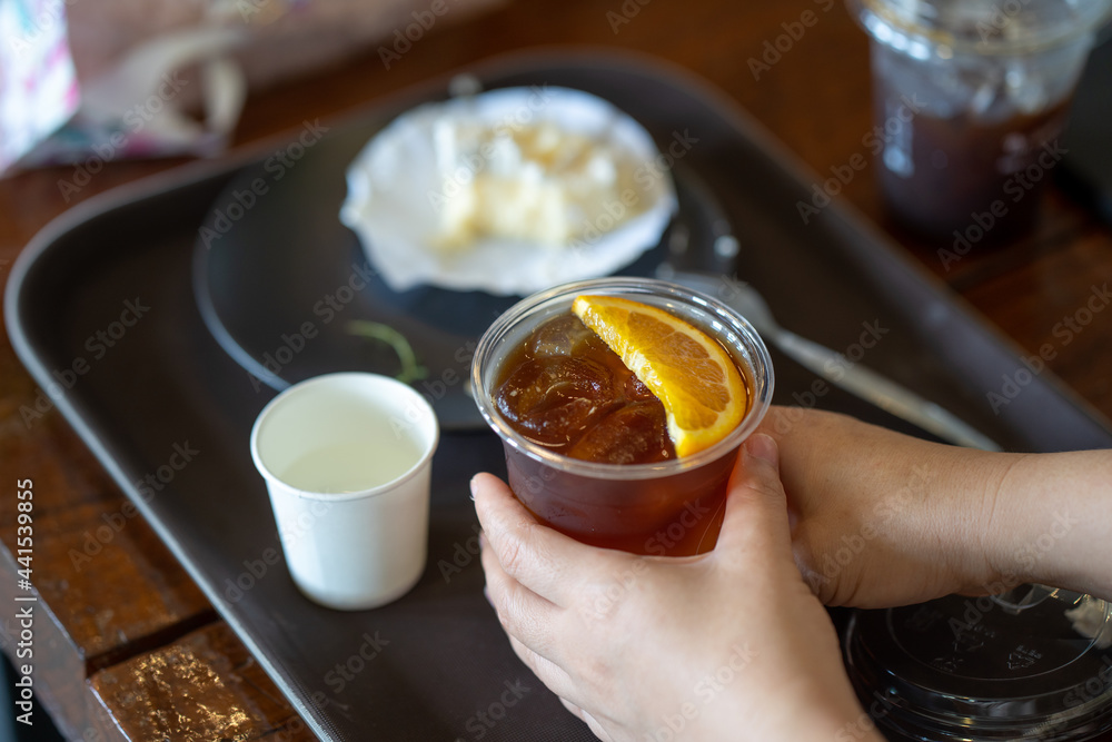 Top view hands holding ice Americano orange coffee at table. Top view hands holding ice Americano orange coffee at table.