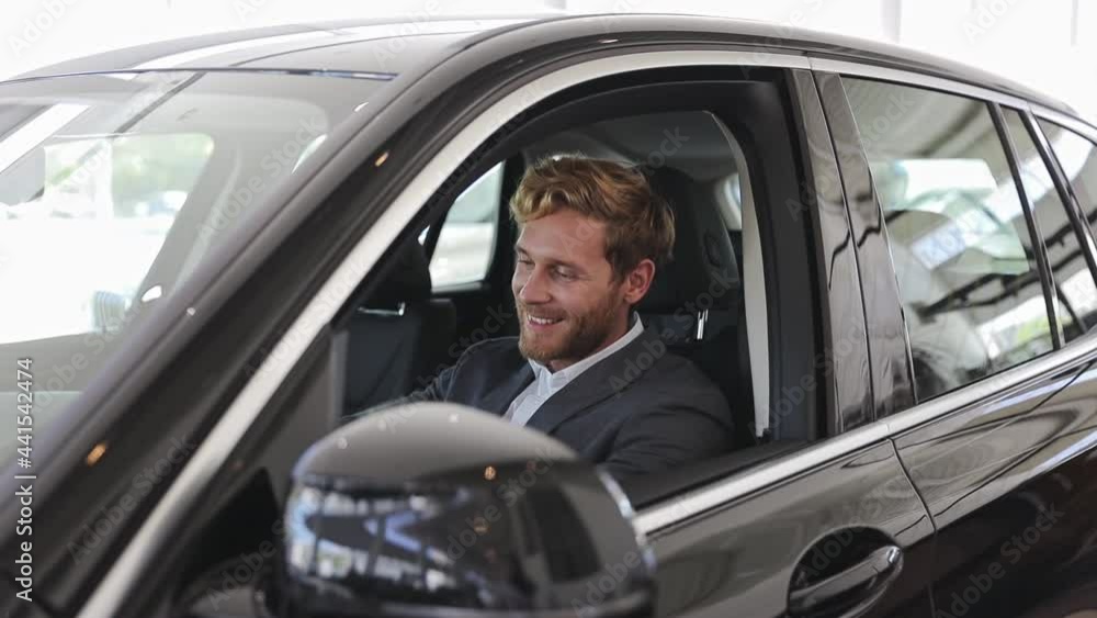 Happy adult man customer male buyer businessman client wears classic suit chooses auto wants to buy new automobile sit in car showroom vehicle salon dealership store motor show indoors. Sales concept Happy adult man customer male buyer businessman client wears classic suit chooses auto wants to buy new automobile sit in car showroom vehicle salon dealership store motor show indoors. Sales concept