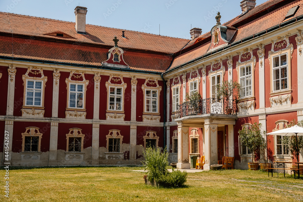 Baroque castle Steknik, stucco, peeling dark red plaster, red tile roof, green lawn, italian garden, aristocratic residence in summer sunny day, ancient chateau Steknik, Czech Republic