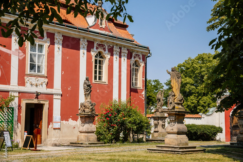 Baroque castle Steknik, stucco, peeling dark red plaster, red tile roof, green lawn, italian garden, aristocratic residence in summer sunny day, ancient chateau Steknik, Czech Republic, June 19 2021