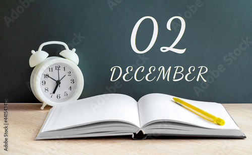 december 02. 02-th day of the month, calendar date.A white alarm clock, an open notebook with blank pages, and a yellow pencil lie on the table.Winter month, day of the year concept