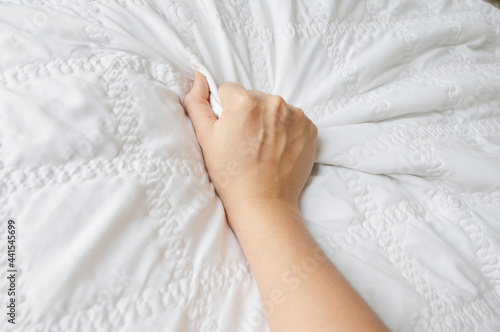 Woman hand gripping hard with visible blood vein on white bed sheet.