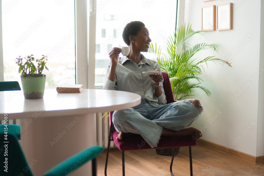 A smiling African American woman is relaxing alone with a cup of coffee at home. A smiling African American woman is relaxing alone with a cup of coffee at home.