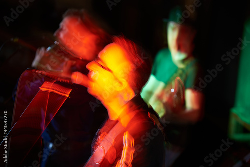 A male musician sings into a microphone and plays the guitar at a concert. Blurry motion. © dvoinik