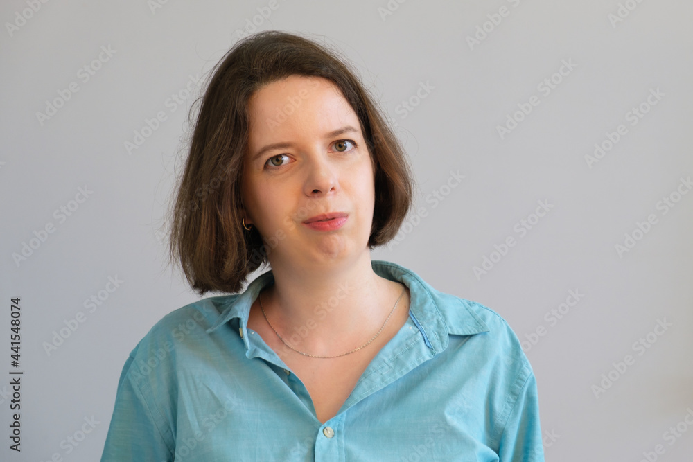 Simple portrait of young brunette woman in blue shirt on gray wall background. Business portrait of employee, manager, casual business dress. Photo of employee. Serious woman without emotion Simple portrait of young brunette woman in blue shirt on gray wall background. Business portrait of employee, manager, casual business dress. Photo of employee. Serious woman without emotion