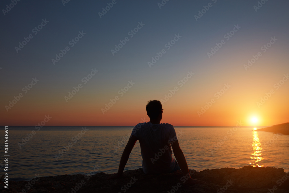 Silhouette of a man watching sunset over distant horizon.