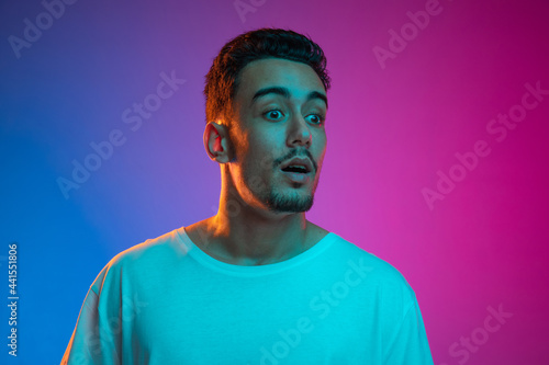 Portrait of Latina young man posing isolated on gradient purple pink background in neon light. Front view