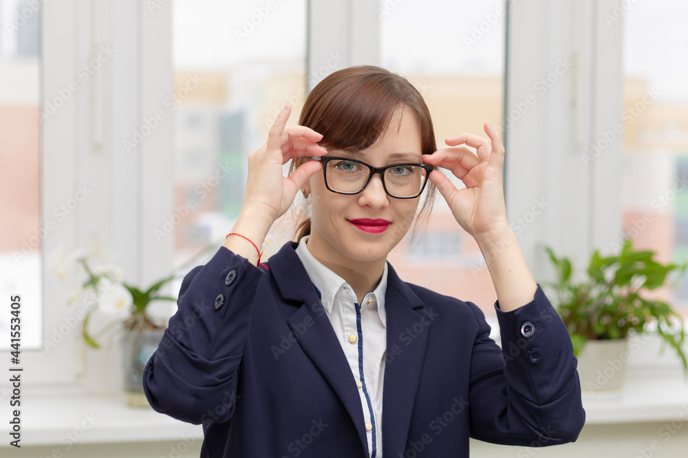 young stylish pretty business woman in a blue jacket and glasses by the window in the office at her workplace is satisfied with the work done young stylish pretty business woman in a blue jacket and glasses by the window in the office at her workplace is satisfied with the work done