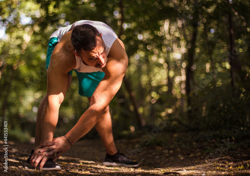 Young sports man stretching in the forest.