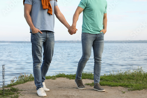 Gay couple walking near river on sunny day, closeup