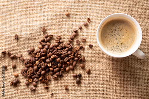 Cup of coffee with roasted coffee beans on brown cloth