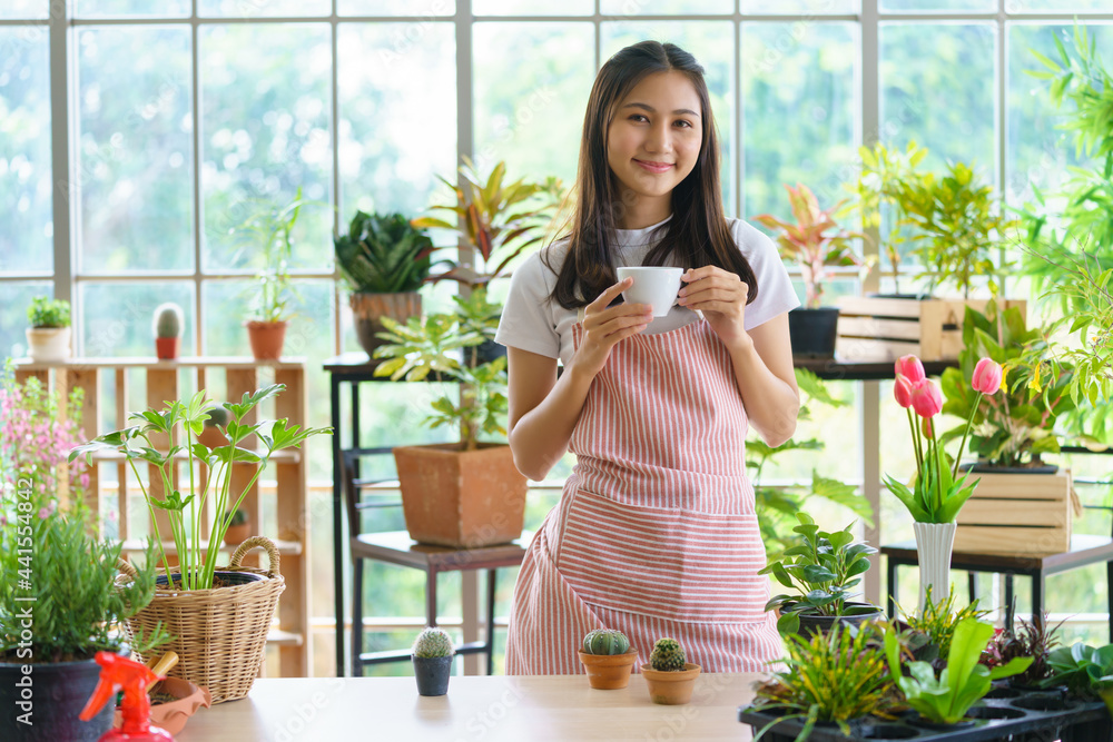 A happy florist gardener in apron holding a coffee cup at the garden nursery. Plant seller, Botanist working in an online floral plant shop. E commerce shopping, Small delivery business from home