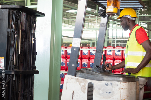 African America worker in safety vest and helmet in forklift machine on storage.
