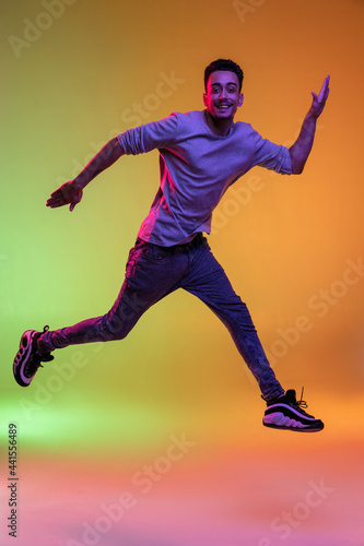 Full length portrait of Latina young man jumping high isolated on gradient yellow green background in neon light.