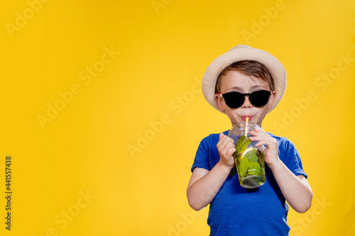 Boy in summer outfit wearing sunglasses and enjoying while drinking a Mojito cocktail. Posing on the yellow background.