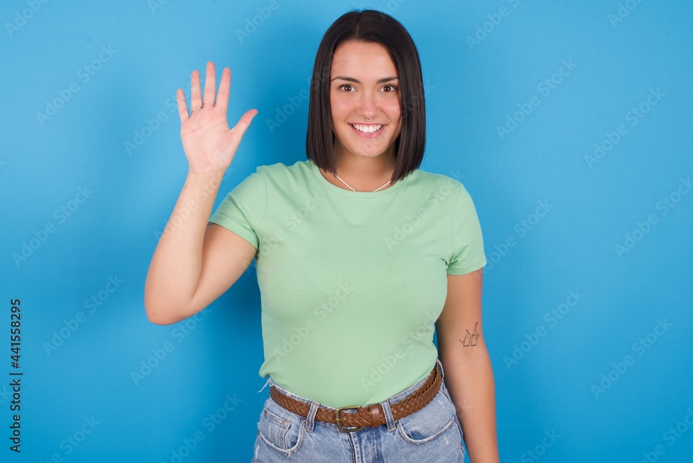 young beautiful brunette girl with short hair standing against blue background showing and pointing up with fingers number five while smiling confident and happy. young beautiful brunette girl with short hair standing against blue background showing and pointing up with fingers number five while smiling confident and happy.