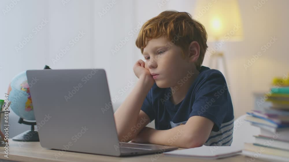 Exhausting home schooling. Cute little redhead boy feeling tired, yawning while watching online lessons on laptop Exhausting home schooling. Cute little redhead boy feeling tired, yawning while watching online lessons on laptop