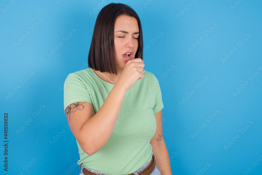 young beautiful brunette girl with short hair standing against blue background feeling unwell and coughing as symptom for cold or bronchitis. Healthcare concept. young beautiful brunette girl with short hair standing against blue background feeling unwell and coughing as symptom for cold or bronchitis. Healthcare concept.