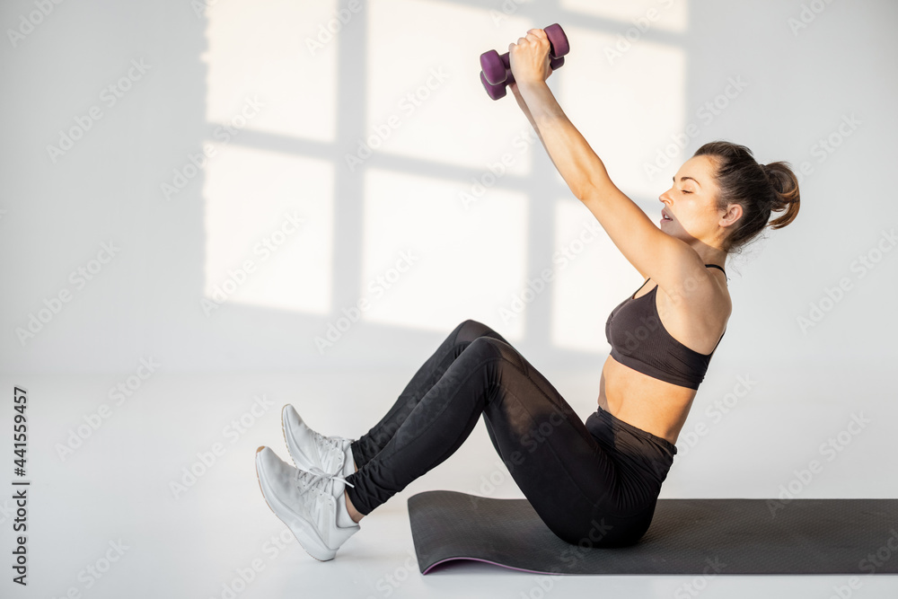 Obraz premium Beautiful and confident athletic woman doing cardio with dumbbells at white room. Training fitness or aerobics alone