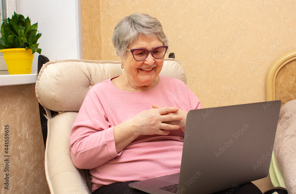 Senior lady sits in a chair and looks at the laptop screen with a joyful smile Senior lady sits in a chair and looks at the laptop screen with a joyful smile