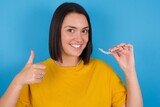 young beautiful brunette girl with short hair holding an invisible braces aligner and rising thumb up, recommending this new treatment. Dental healthcare concept.