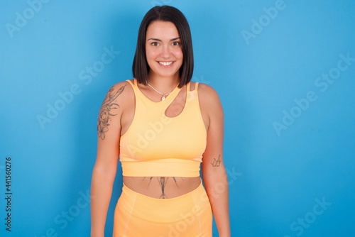 young beautiful sporty girl standing against blue background with nice beaming smile pleased expression. Positive emotions concept