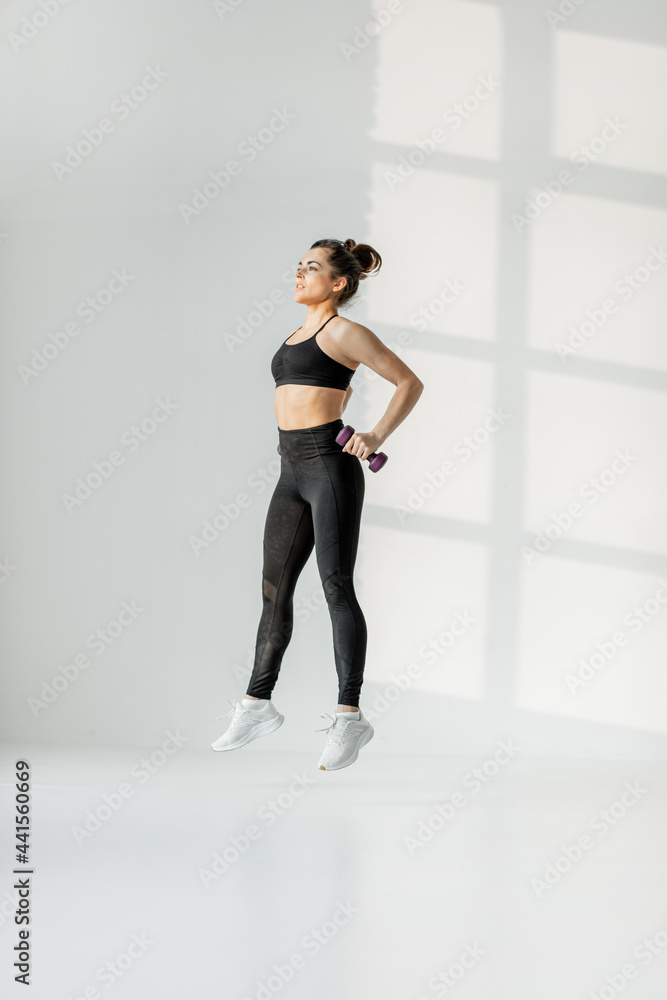 Beautiful and confident athletic woman doing cardio, juming with dumbbells at white room. Training fitness or aerobics alone Beautiful and confident athletic woman doing cardio, juming with dumbbells at white room. Training fitness or aerobics alone