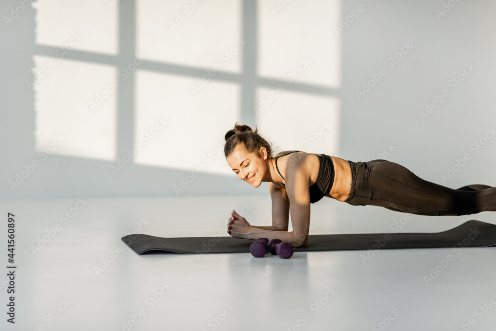 Athletic woman stands in the plank on a fitness matt, performing static exercise on a fitness training at white room alone