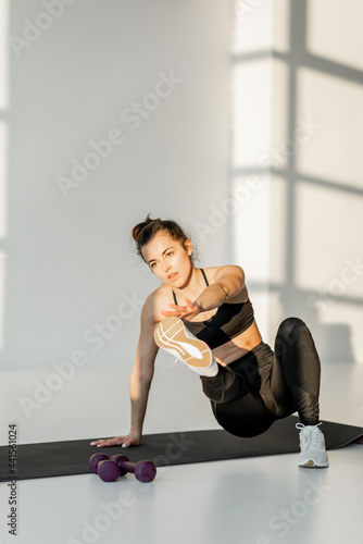 Beautiful athletic woman doing lunges and squats during a fitness training at white sunny room alone