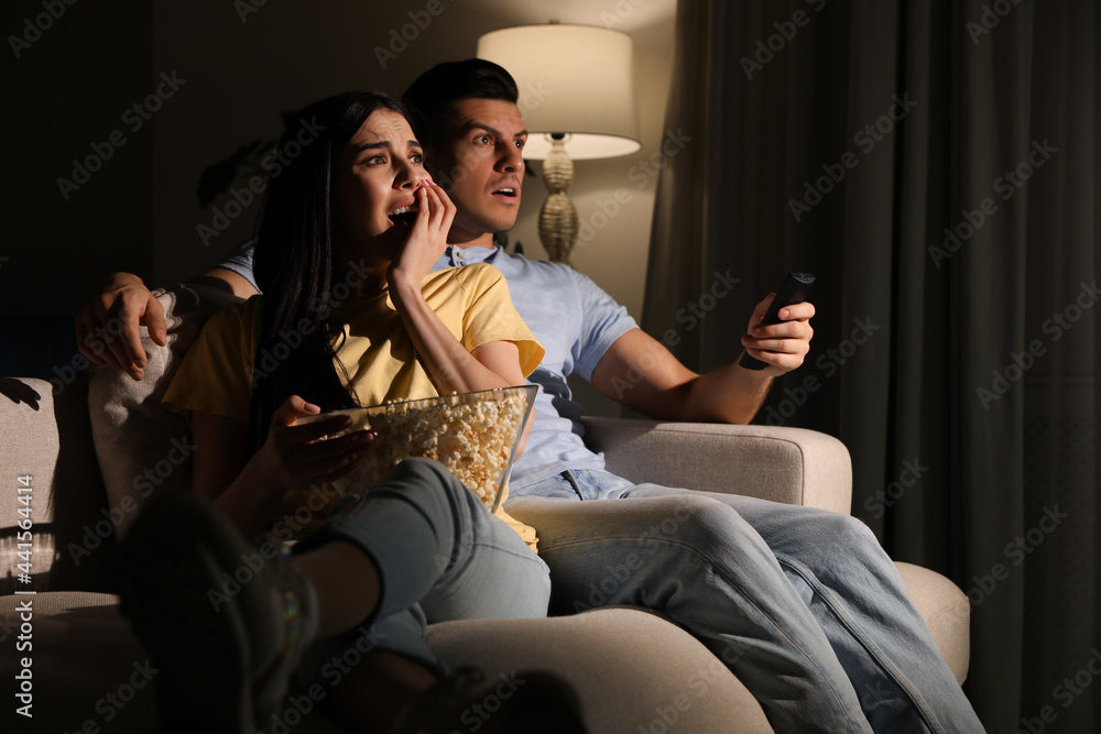 Couple watching movie with popcorn on sofa at night Couple watching movie with popcorn on sofa at night