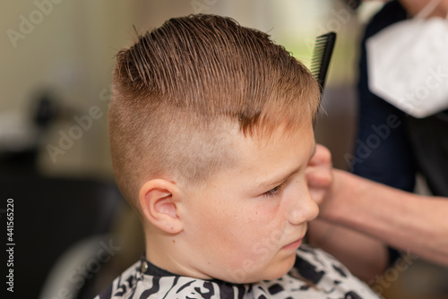 Cute kid boy have hair cut, professional barber doing haircut. Hairdress for children. side view portrait barbershop.