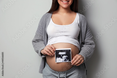Young pregnant woman with ultrasound picture of baby on grey background, closeup