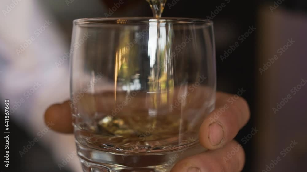 A simple working man with a hand with dirt near his nails holds a clear glass and pours a delicious alcoholic strong drink from a bottle. Gourmet expensive drinks. A simple working man with a hand with dirt near his nails holds a clear glass and pours a delicious alcoholic strong drink from a bottle. Gourmet expensive drinks.