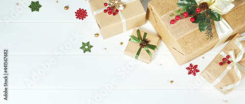 Christmas banner with gift boxes border wrapped in kraft paper decorated with red berries and Christmas greenery on white wood desk background. Xmas, winter, holiday concept. Flat lay, copy space