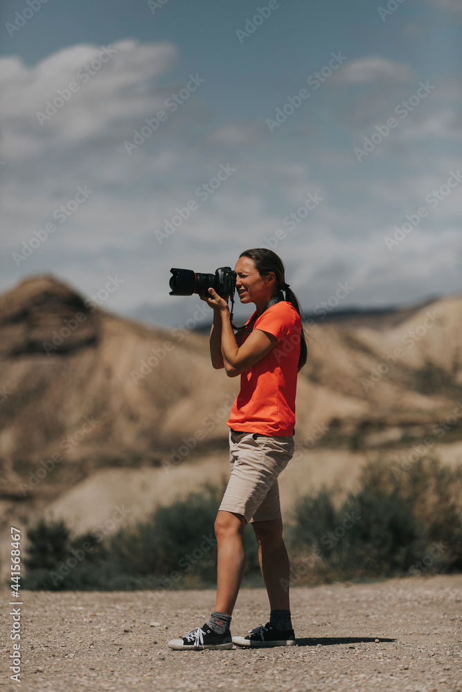 Woman photographer framing for taking photos in Tabernas Desert, Spain, in a sunny day, with an orange color t-shirt.