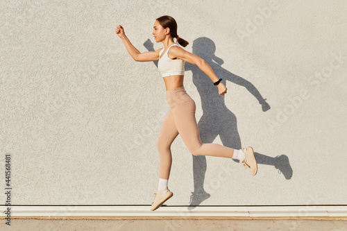 Portrait of fit sporty girl jumping over in the air looking straight ahead, having good stretching isolated on gray background outdoor, life, energy, lifestyle.