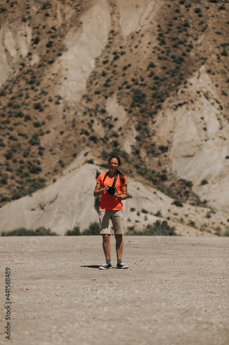 Woman photographer taking photos in Tabernas Desert, Spain, in a sunny day, with an orange color t-shirt.