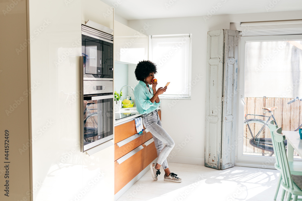 Woman eating fruit and browsing smartphone at home Woman eating fruit and browsing smartphone at home
