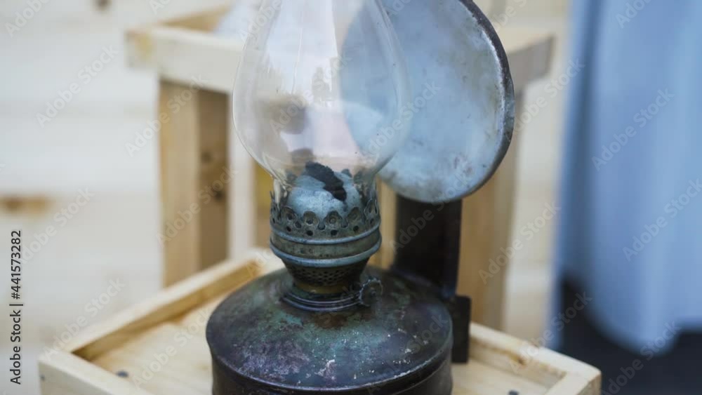 An old vintage kerosene lamp with a mirror plate stands on a wooden stand as an element of wedding decor next to the candles. Ancient times without light. Metal illuminator. Close-up