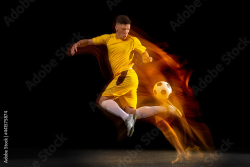 One caucasian male football or soccer player training with ball in mixed light isolated on dark background. Concept of professional sport, active, motion..