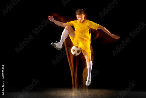 One caucasian male football or soccer player training with ball in mixed light isolated on dark background. Concept of professional sport, active, motion.