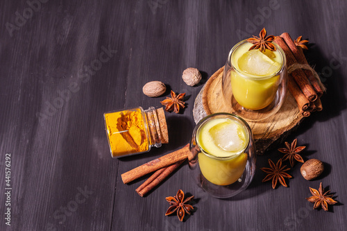 Golden turmeric milk with ice on black wooden background