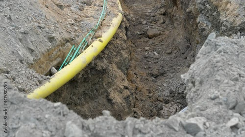 Cables in the ground at construction site. A construction site with an excavated ditch with plastic pipes for electricity and fiber and a cement well.