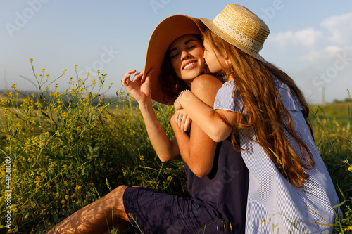 young mom and her wonderful daughter have fun outdoors wearing dresses and straw hats