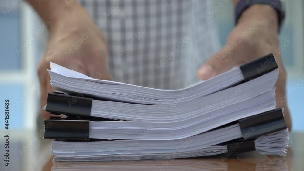 Man walked into the room to raise a pile of papers or stack of documents on the table.