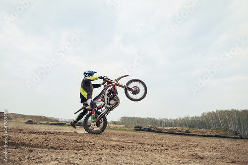 Motorcyclist jumping and riding on rear wheel at enduro motocross training ground